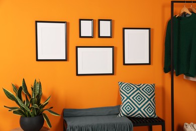 Photo of Empty frames hanging on orange wall in stylish room. Mockup for design