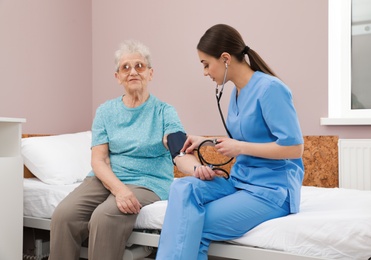 Photo of Nurse measuring senior woman's blood pressure in hospital ward. Medical assisting