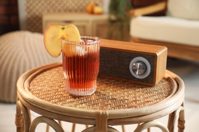 Photo of Glass of tasty cider and portable speaker on wicker table in room. Relax at home