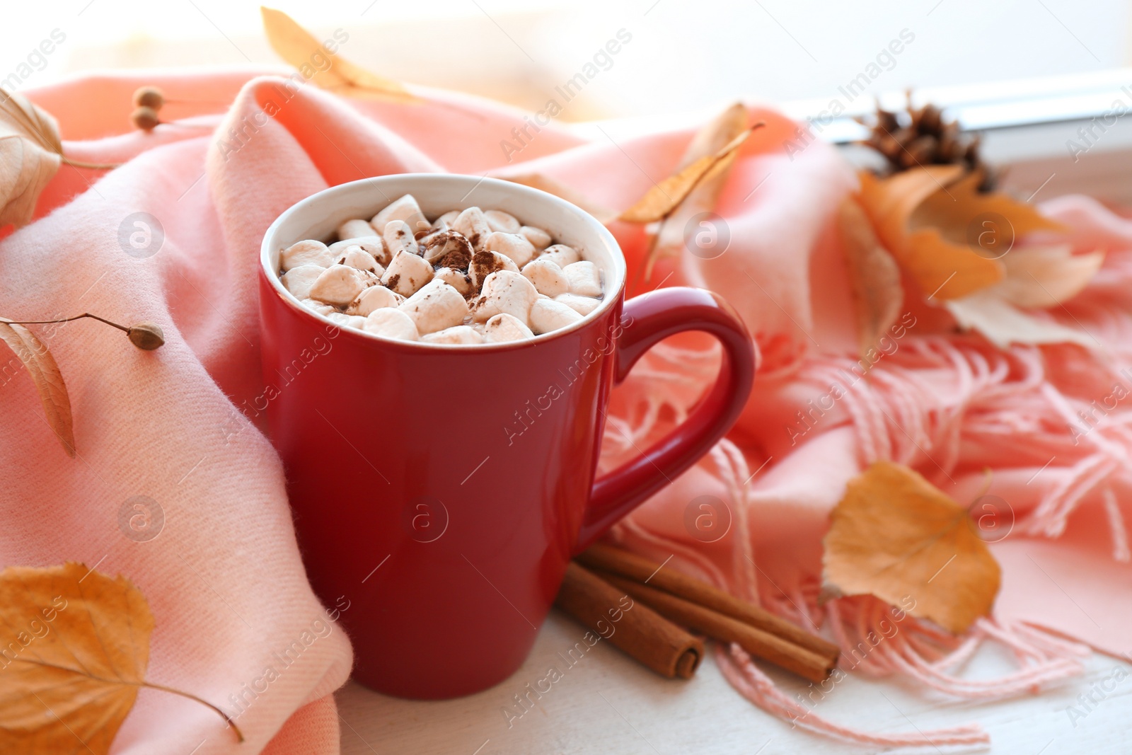 Photo of Cup of hot drink, scarf and autumn leaves on windowsill. Cozy atmosphere