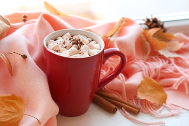 Photo of Cup of hot drink, scarf and autumn leaves on windowsill. Cozy atmosphere