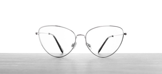 Photo of Stylish glasses with metal frame on table against white background