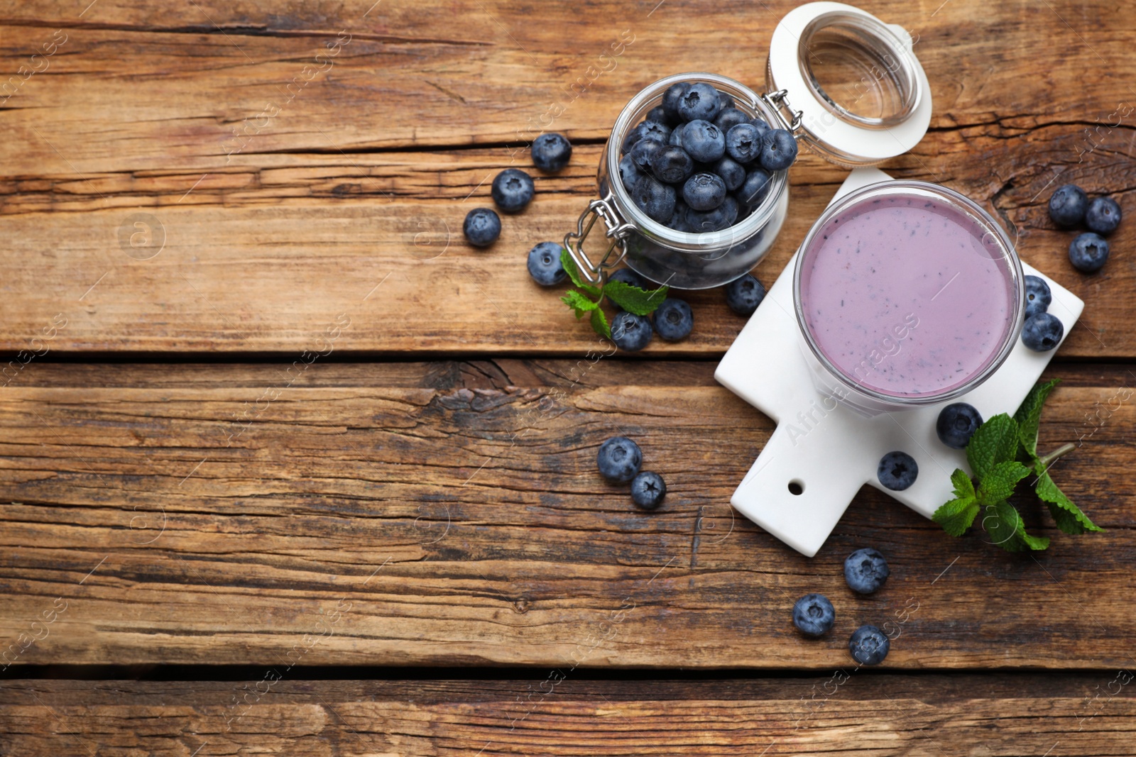 Photo of Glass of blueberry smoothie with mint and fresh berries on wooden table, flat lay. Space for text