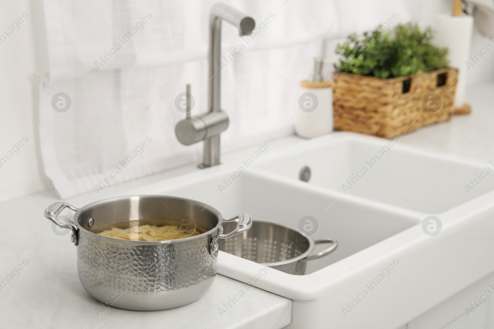 Photo of Cooked pasta in metal pot on countertop near sink. Space for text