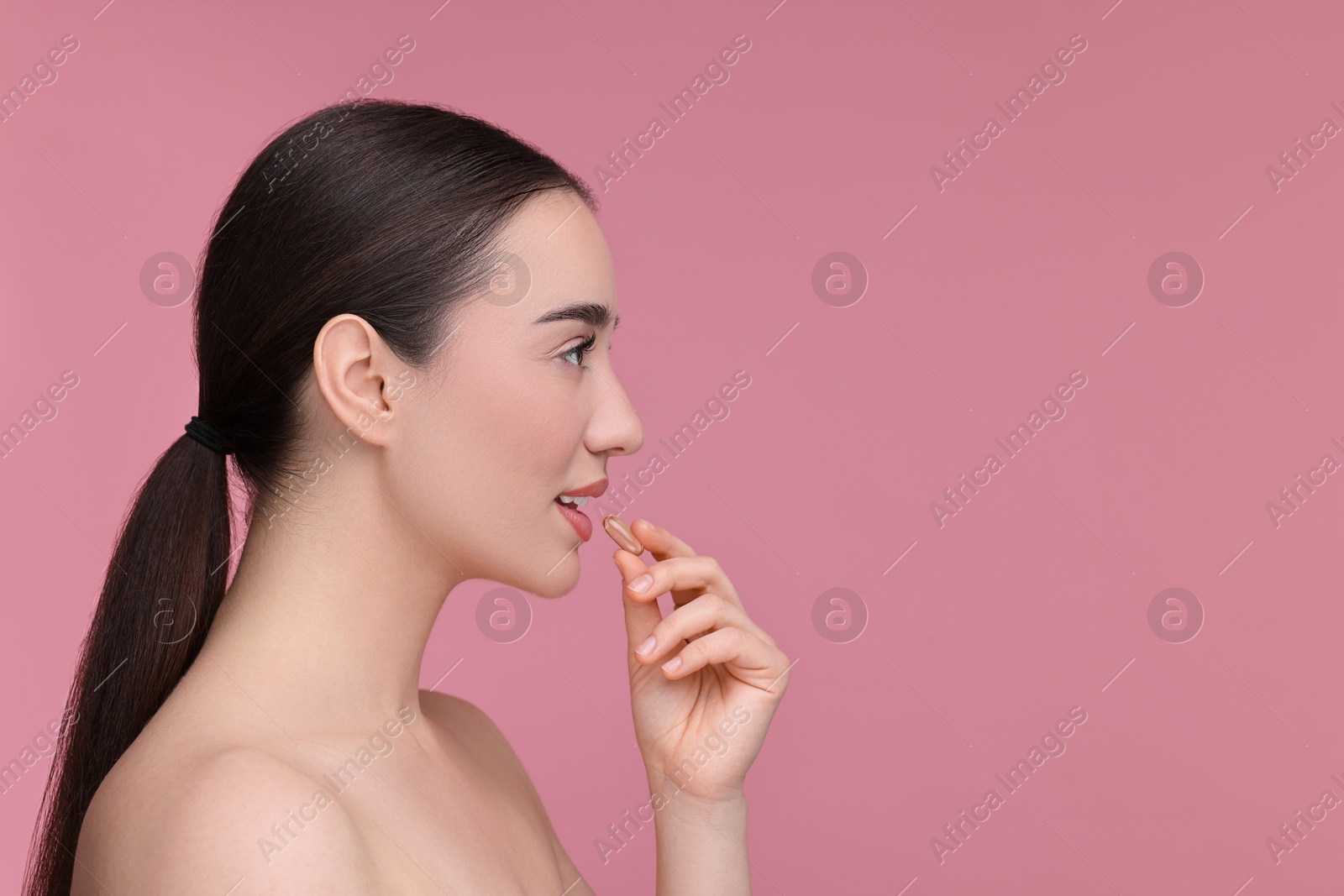 Photo of Beautiful young woman with vitamin pill on pink background. Space for text