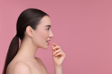 Photo of Beautiful young woman with vitamin pill on pink background. Space for text