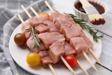 Photo of Skewers with pieces of raw meat, rosemary, tomatoes and marinade on rustic wooden table, closeup