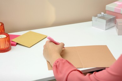 Photo of Young woman writing message in greeting card at white table, closeup