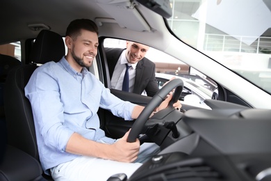 Photo of Salesman consulting young man in auto at dealership. Buying new car