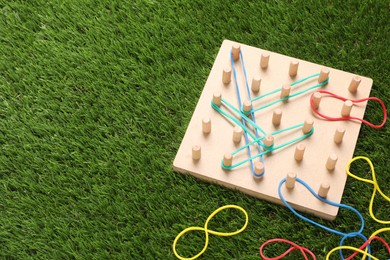Photo of Wooden geoboard with rubber bands on artificial grass, above view and space for text. Educational toy for motor skills development