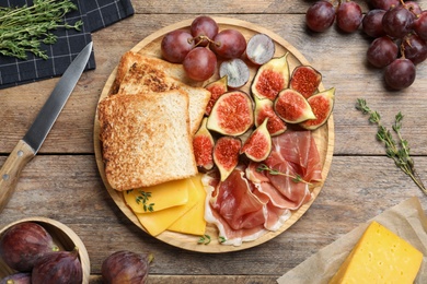 Photo of Delicious ripe figs, prosciutto and cheese served on wooden table, flat lay