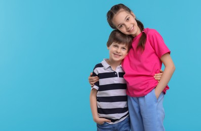 Happy brother and sister hugging on light blue background, space for text