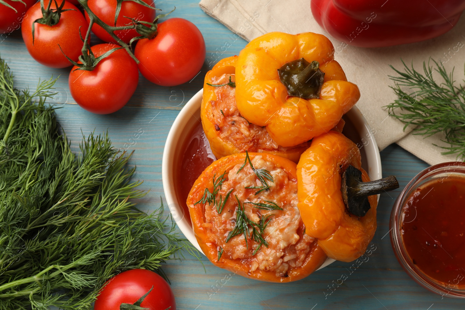 Photo of Tasty stuffed peppers in bowl and products on light blue wooden table, flat lay