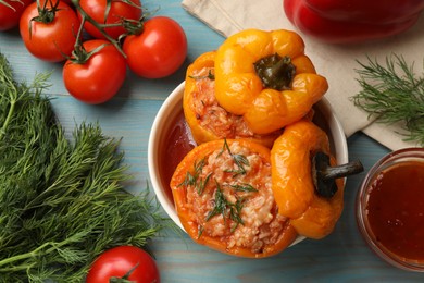 Photo of Tasty stuffed peppers in bowl and products on light blue wooden table, flat lay