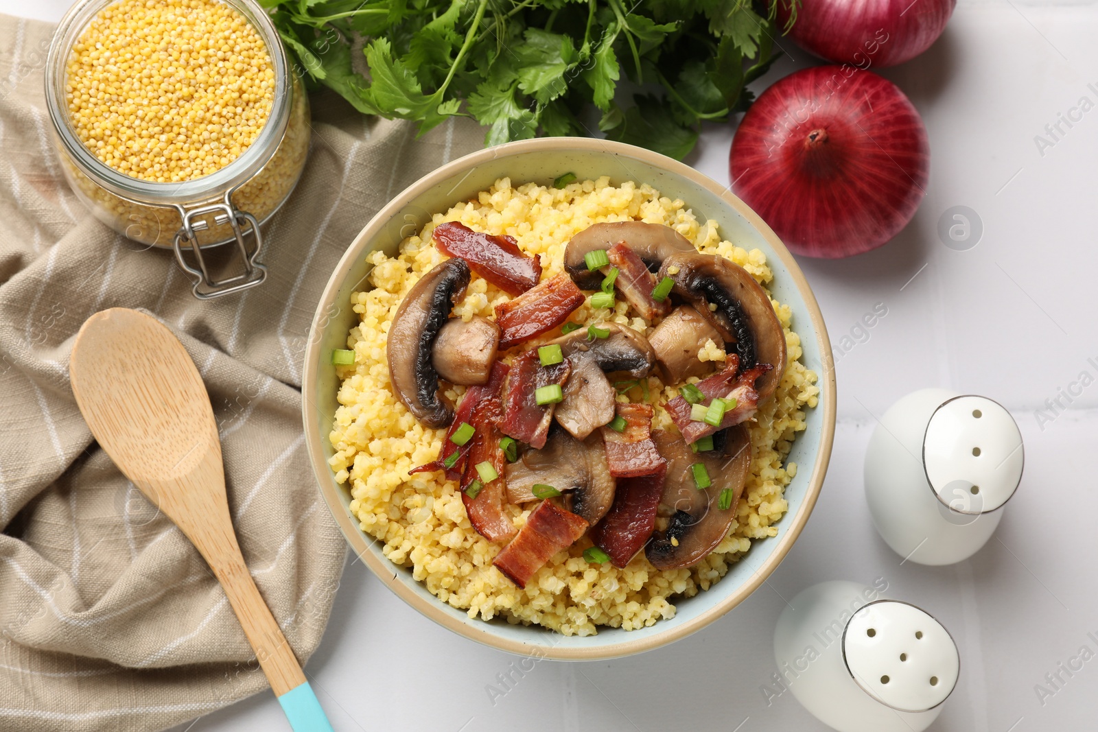 Photo of Tasty millet porridge with mushrooms, bacon and green onion in bowl on white table, flat lay