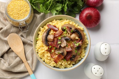 Tasty millet porridge with mushrooms, bacon and green onion in bowl on white table, flat lay