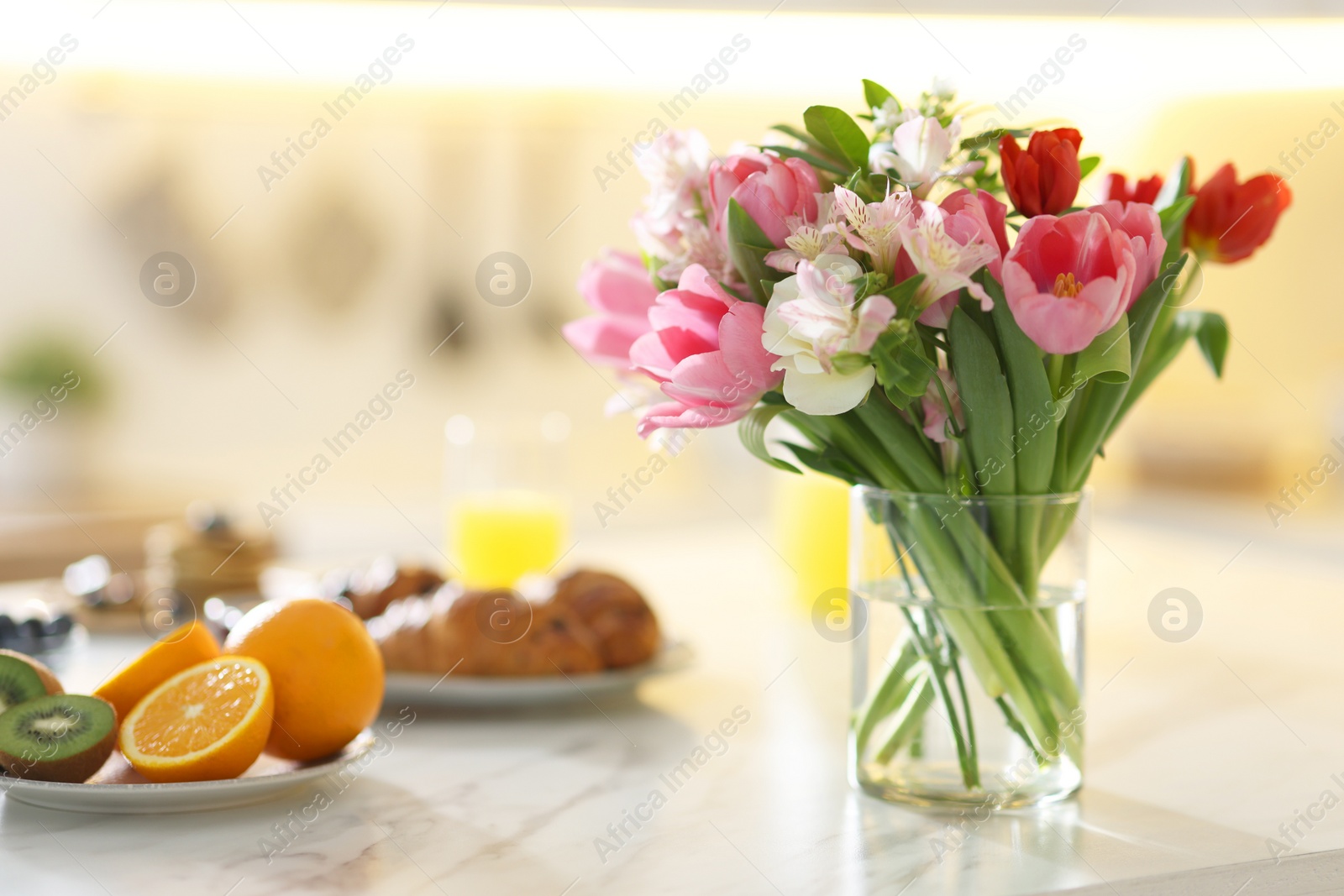 Photo of Bouquet of beautiful flowers in vase and food for breakfast on white marble table, closeup