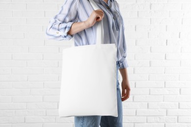 Woman with white textile bag near brick wall, closeup. Space for design