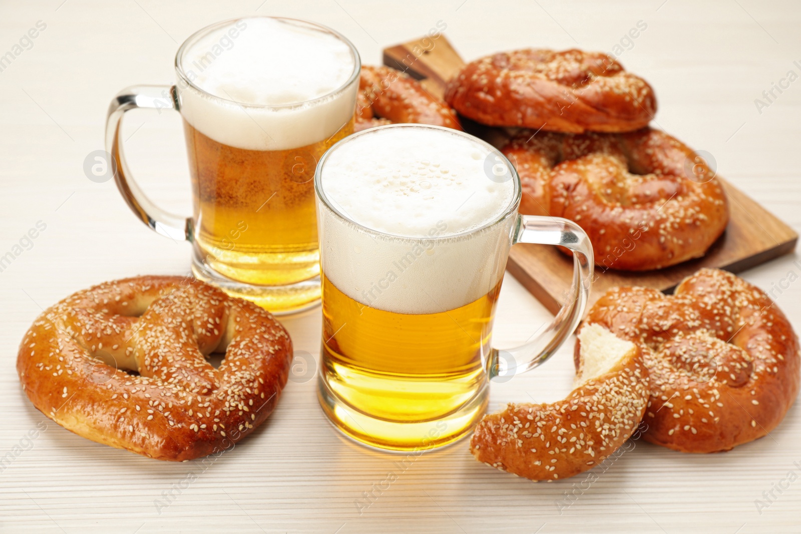 Photo of Tasty pretzels and glasses of beer on white wooden table