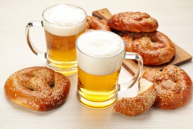 Tasty pretzels and glasses of beer on white wooden table