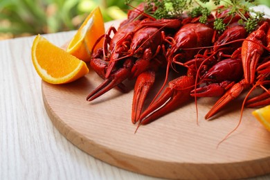 Photo of Delicious red boiled crayfish and orange on white wooden table
