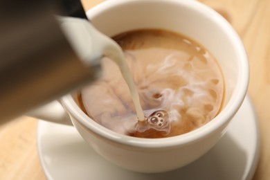 Photo of Pouring milk into cup at table, closeup