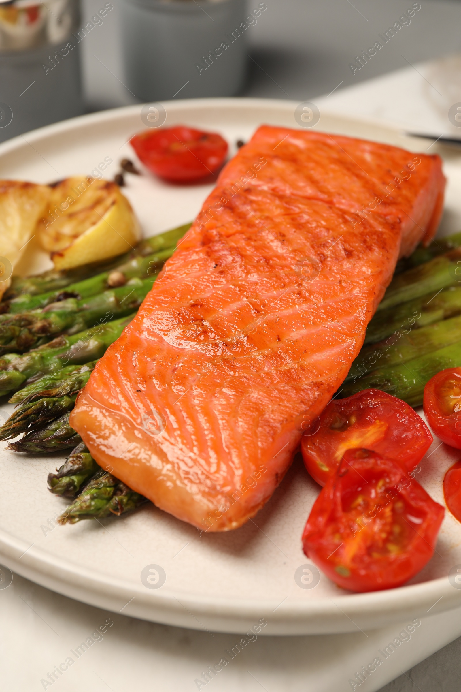 Photo of Tasty grilled salmon with asparagus, tomatoes and lemon on table, closeup