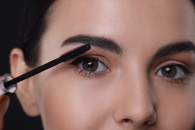 Photo of Beautiful young woman applying mascara on black background, closeup