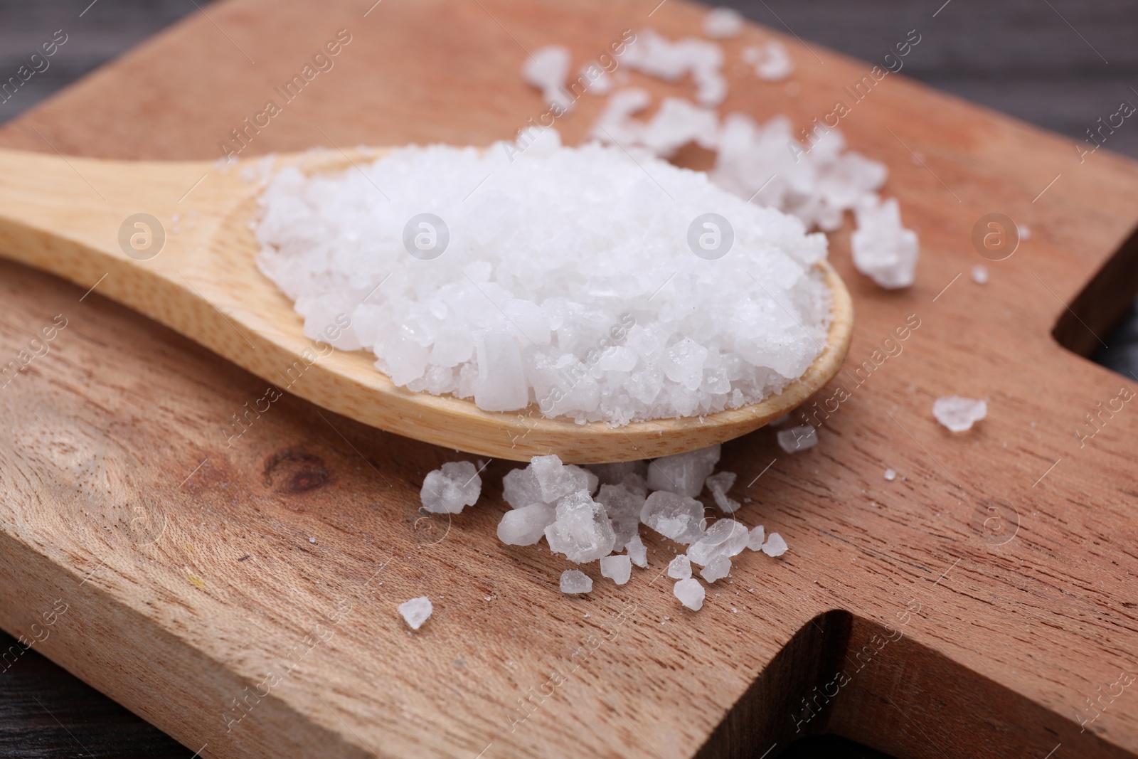 Photo of Spoon with sea salt on wooden board, closeup