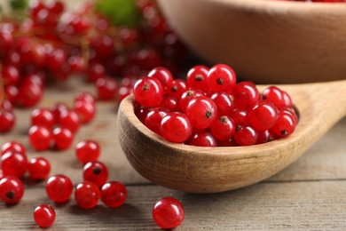 Spoon with ripe red currants on wooden table, closeup