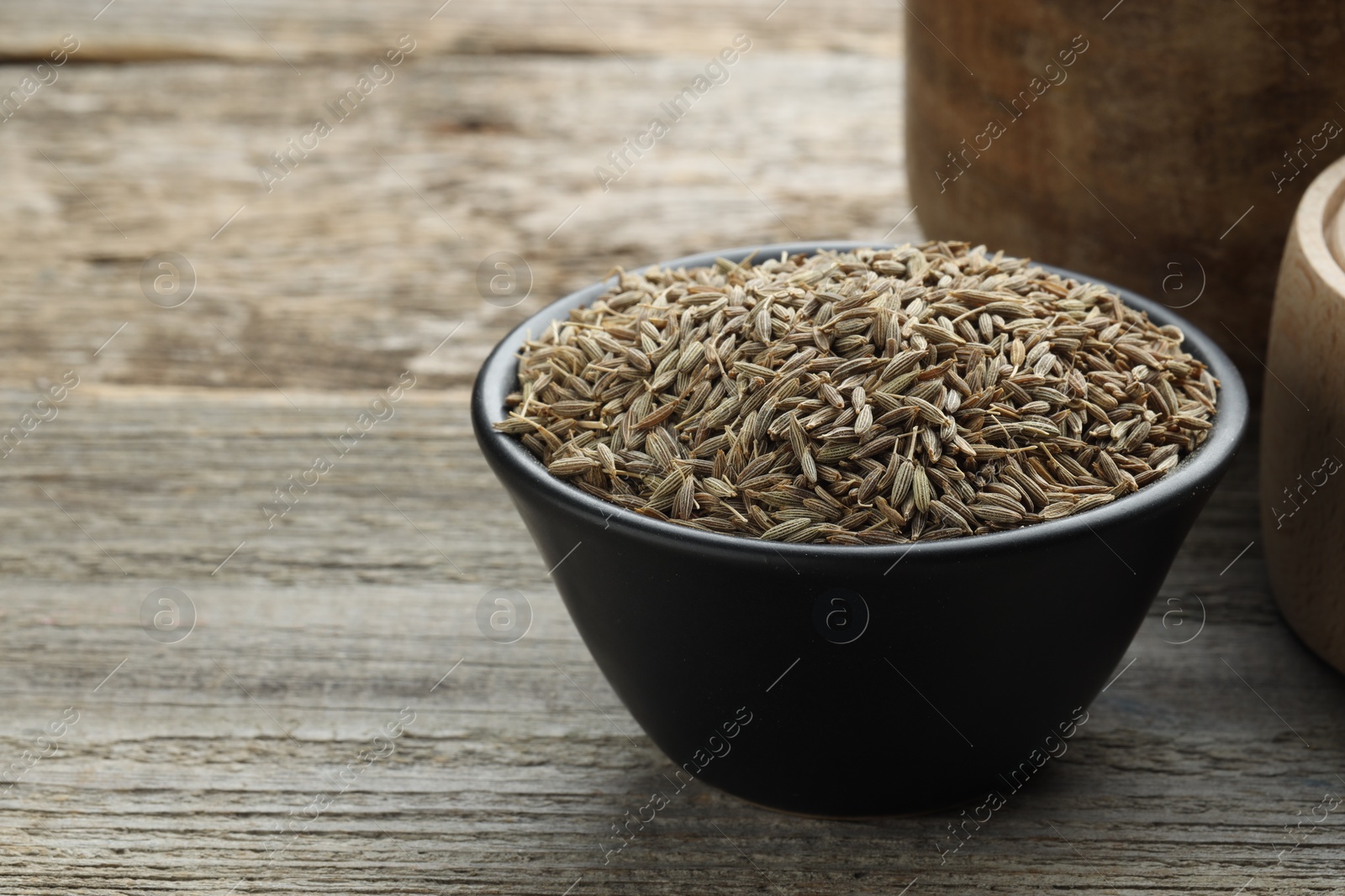 Photo of Bowl of caraway seeds on wooden table, closeup. Space for text