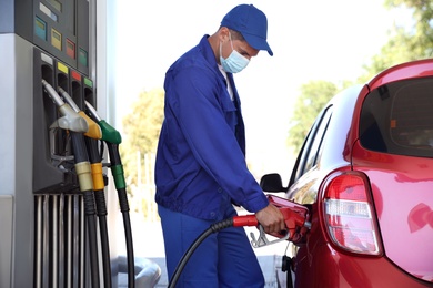 Photo of Worker in mask refueling car at modern gas station