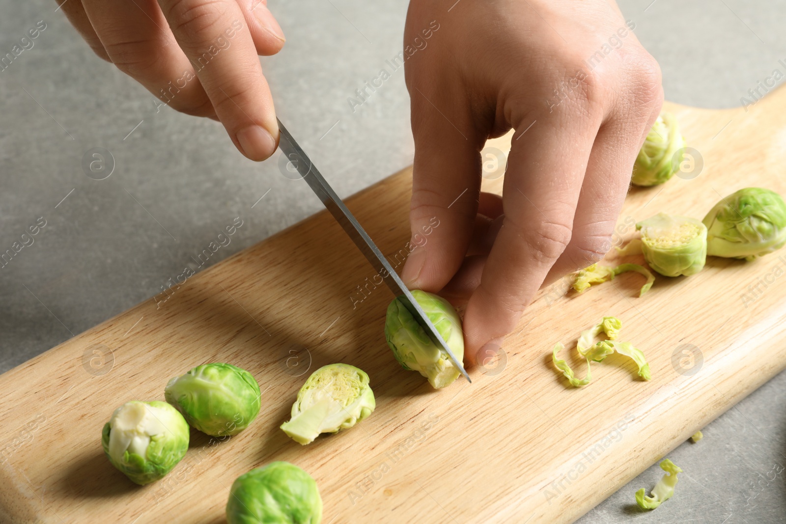 Photo of Woman cutting fresh Brussels sprouts on wooden board, closeup