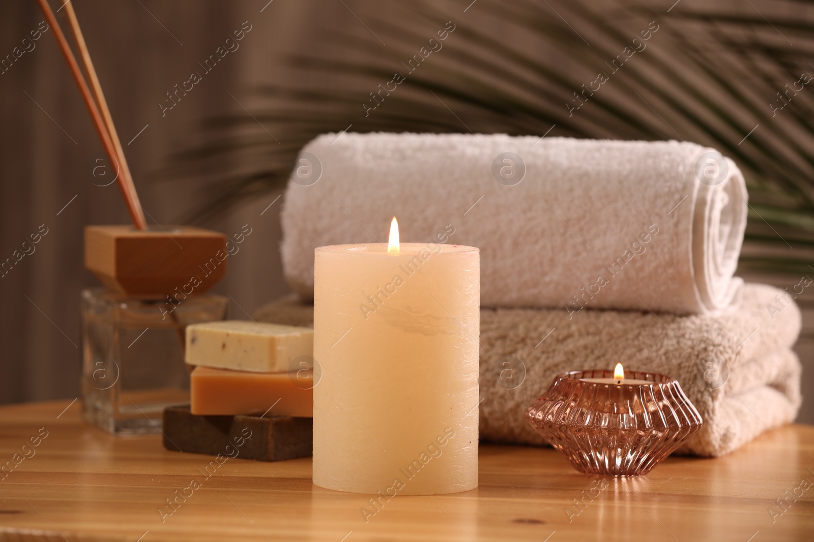 Photo of Spa composition. Burning candles, towels, soap and reed air freshener on wooden table, closeup