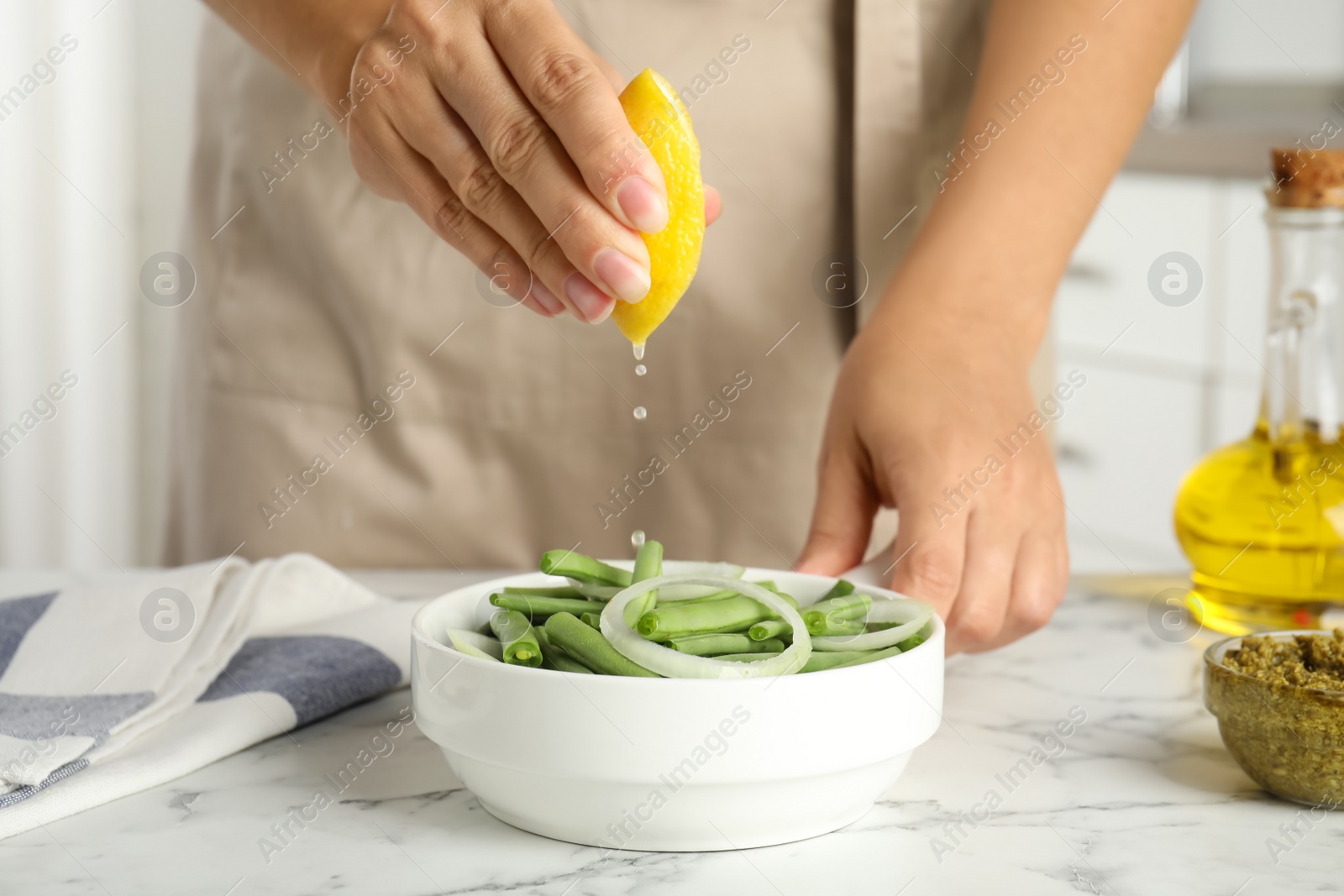 Photo of Woman adding lemon juice to green beans at white marble table, closeup