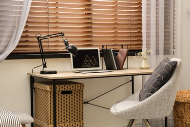 Photo of Comfortable workplace near window with horizontal wooden blinds
