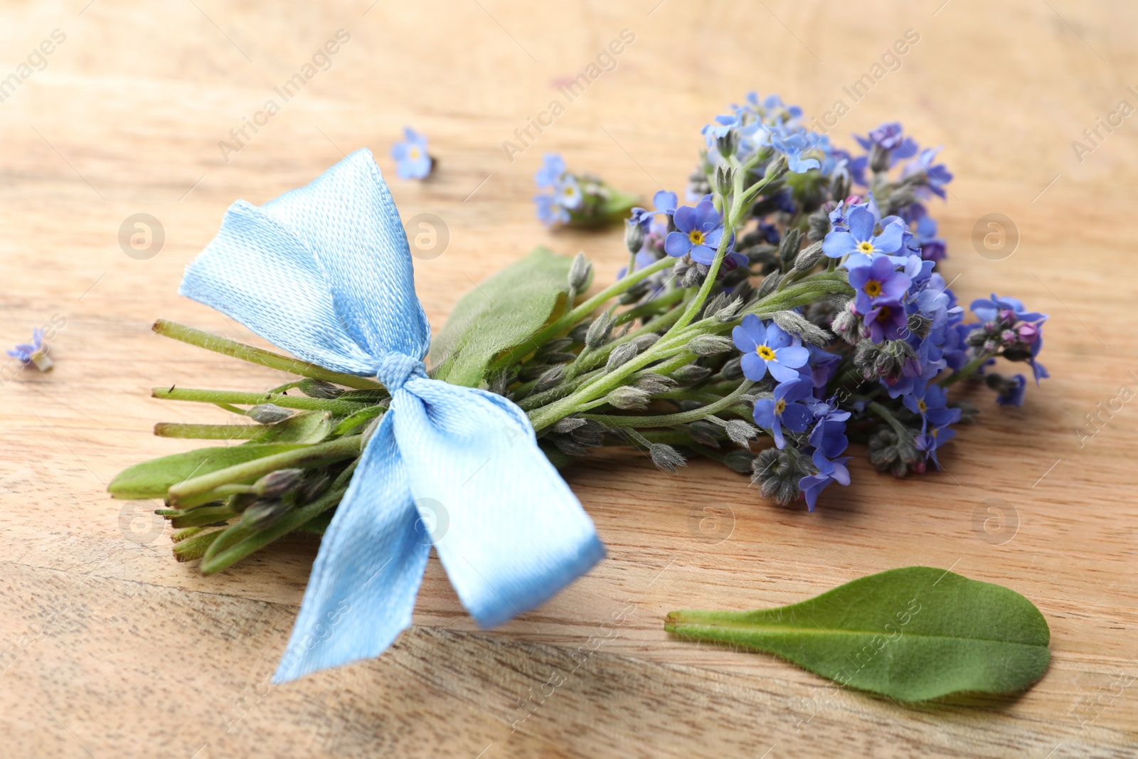 Photo of Beautiful blue forget-me-not flowers tied with ribbon on wooden table, closeup