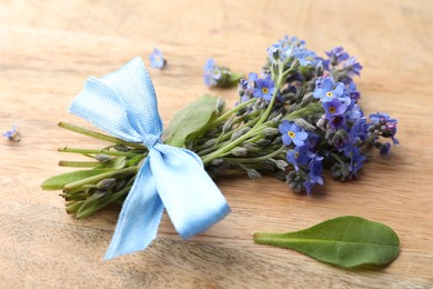 Beautiful blue forget-me-not flowers tied with ribbon on wooden table, closeup