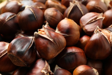 Photo of Pile of delicious edible roasted chestnuts as background, closeup