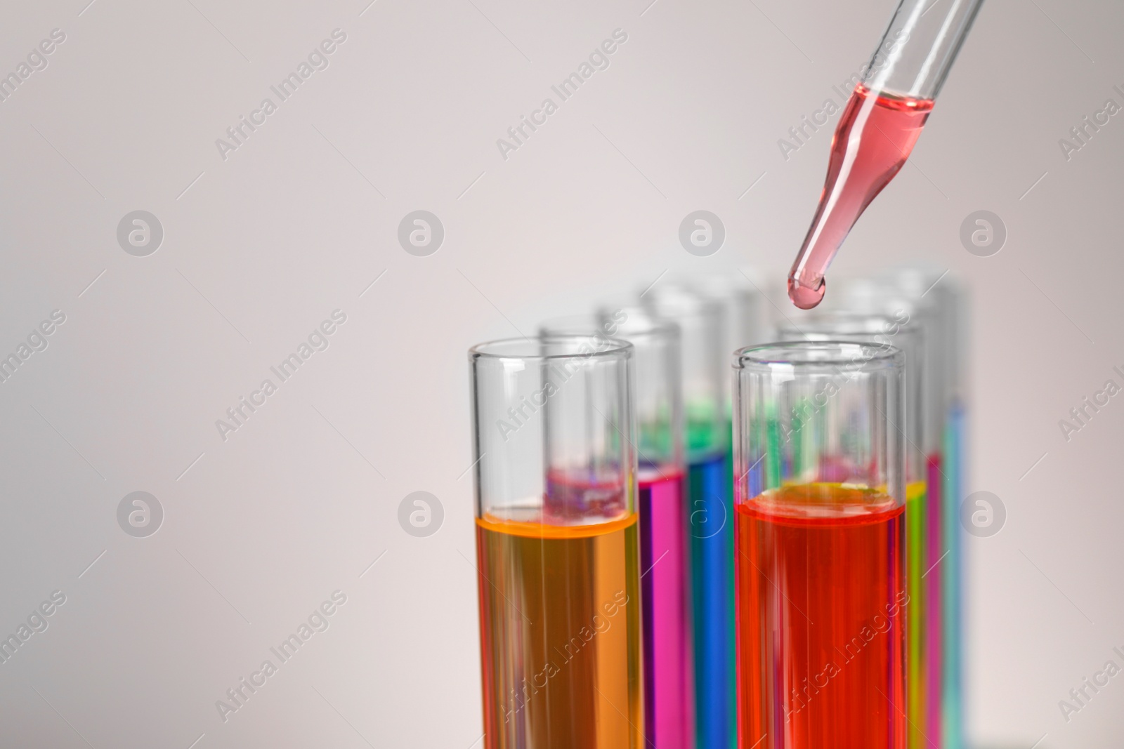 Photo of Dripping liquid from pipette into test tube on grey background, closeup. Space for text