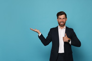 Photo of Smiling bearded man in suit showing thumb up on light blue background. Space for text