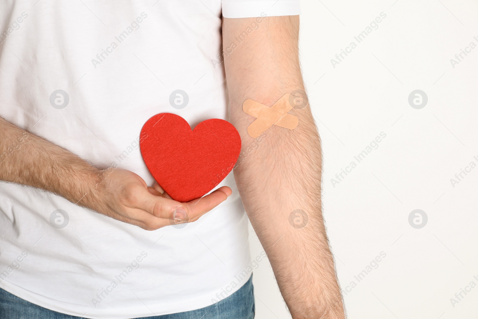 Photo of Man holding fabric heart near hand with adhesive plasters against white background, closeup. Blood donation concept