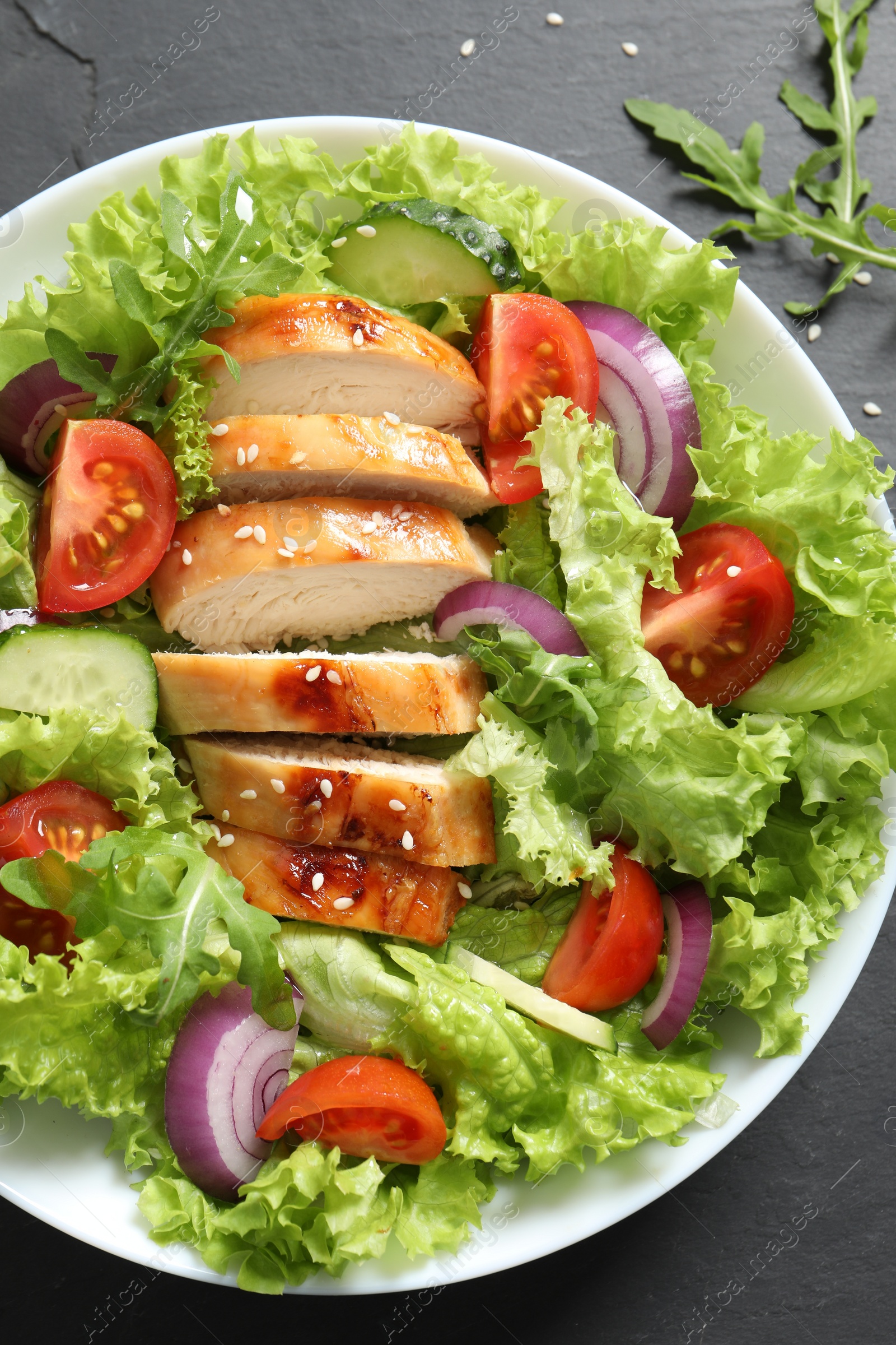 Photo of Delicious salad with chicken and vegetables on black table, top view