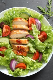 Delicious salad with chicken and vegetables on black table, top view