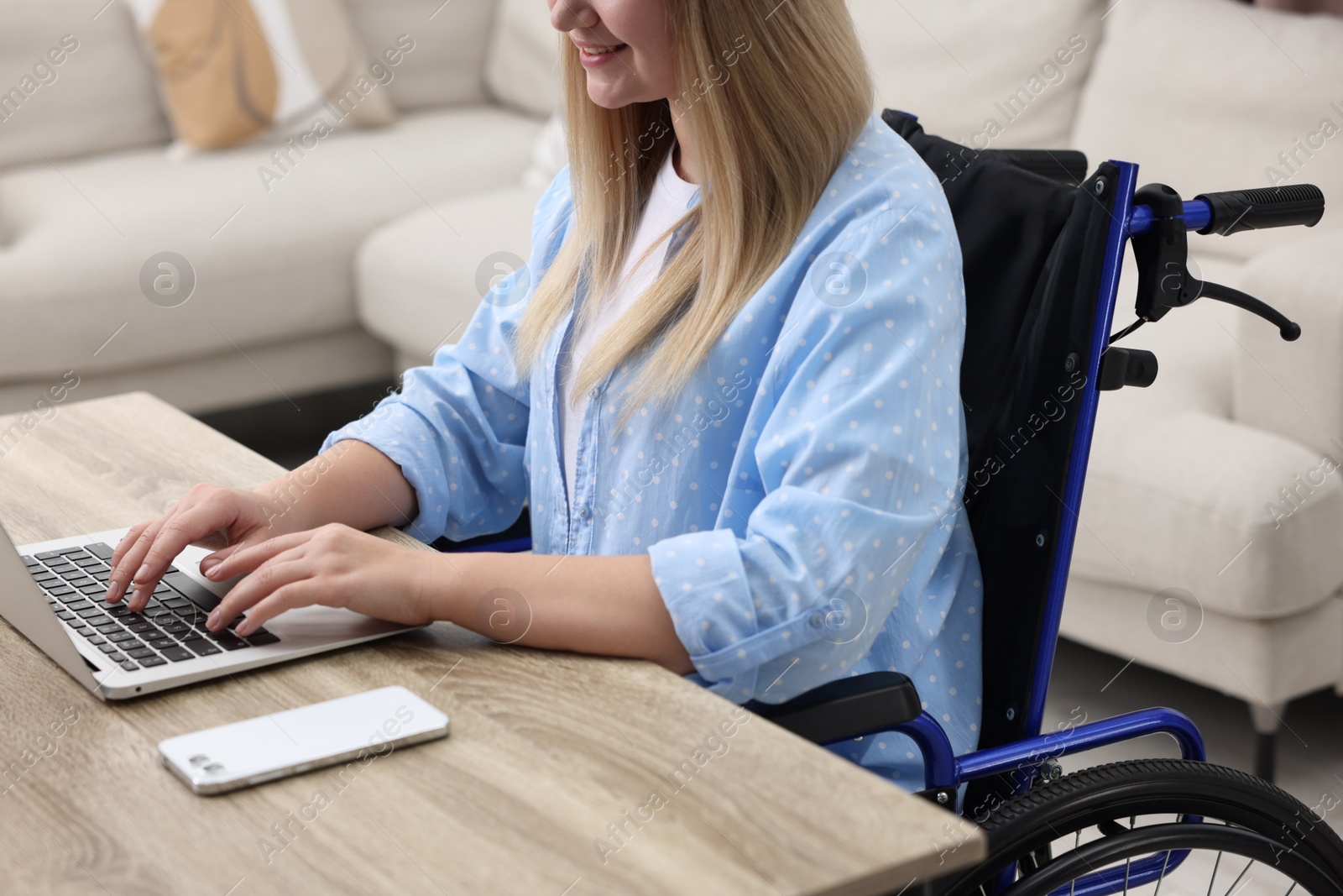 Photo of Woman in wheelchair using laptop at home, closeup