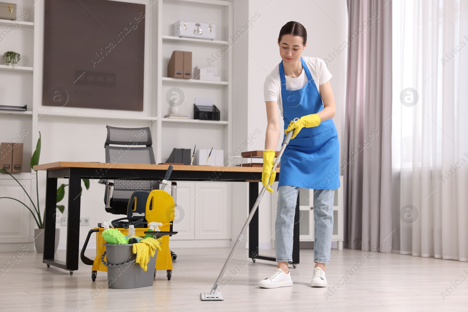 Photo of Cleaning service worker washing floor with mop. Bucket with supplies in office