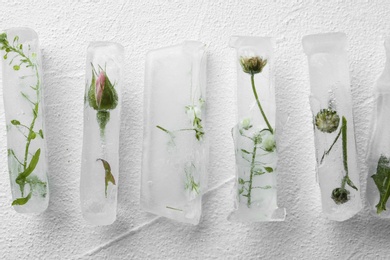 Ice cubes with flowers on white background, flat lay