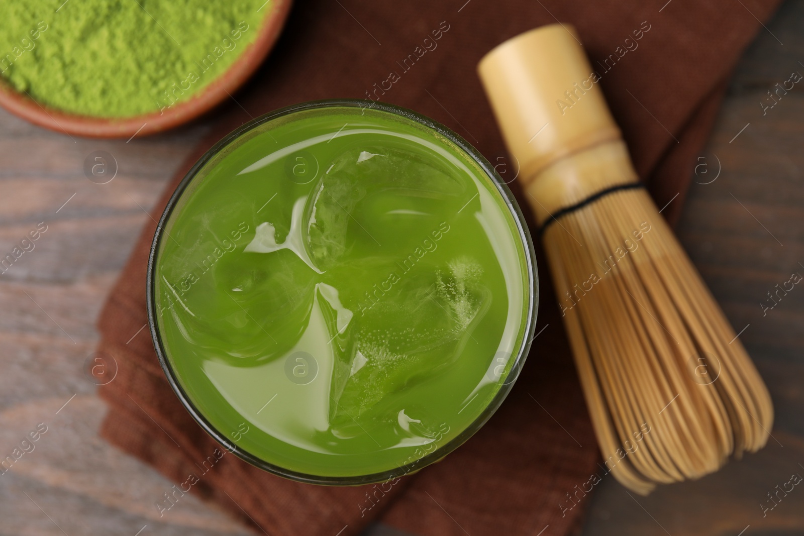 Photo of Glass of delicious iced green matcha tea and bamboo whisk on wooden table, flat lay