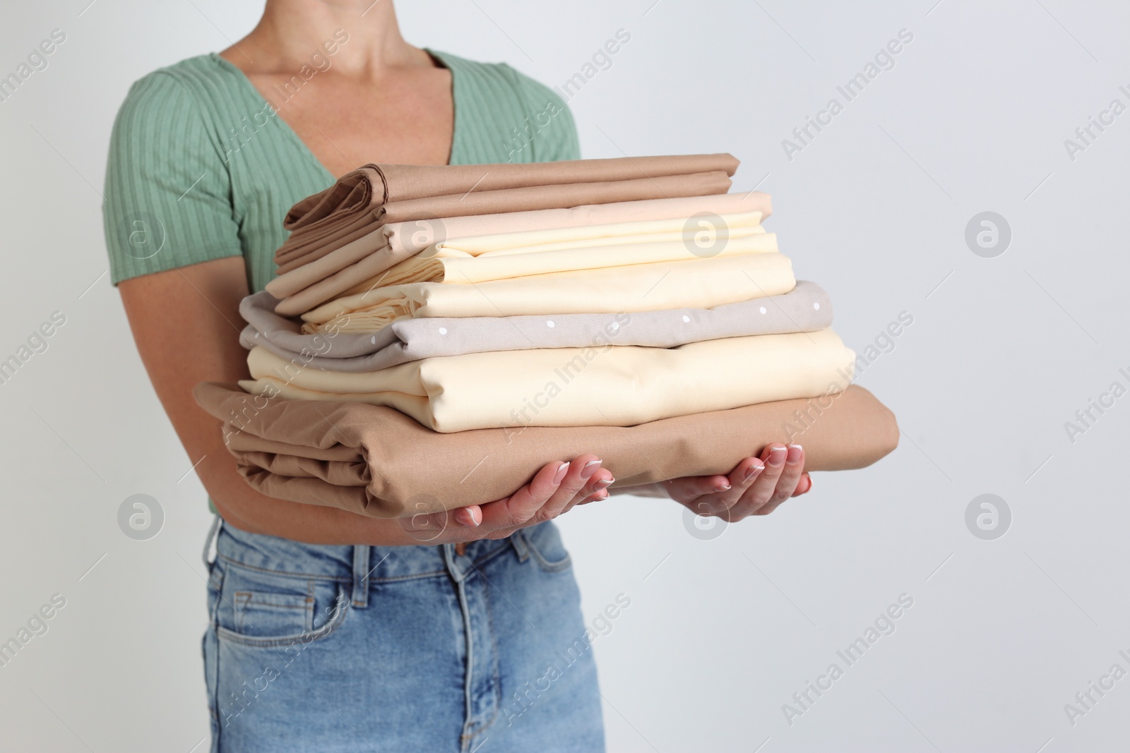 Photo of Woman holding stack of clean bed linens on light grey background