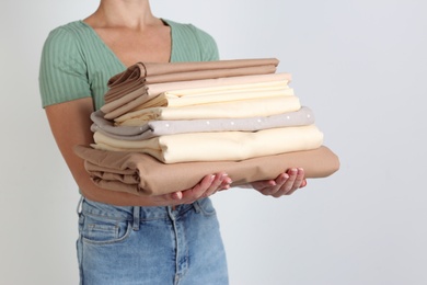 Woman holding stack of clean bed linens on light grey background